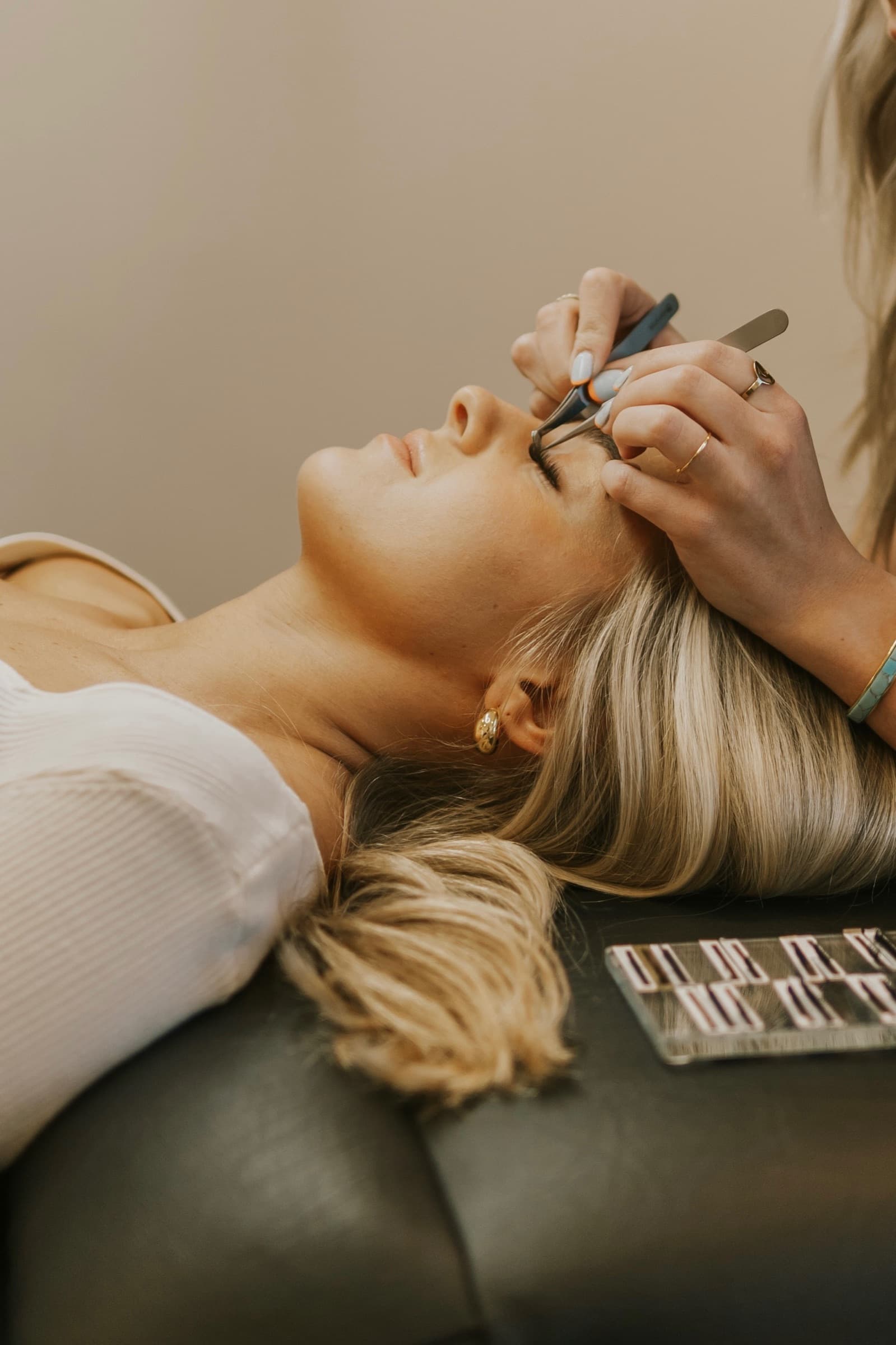 A lash artist applying extensions to a reclining client.