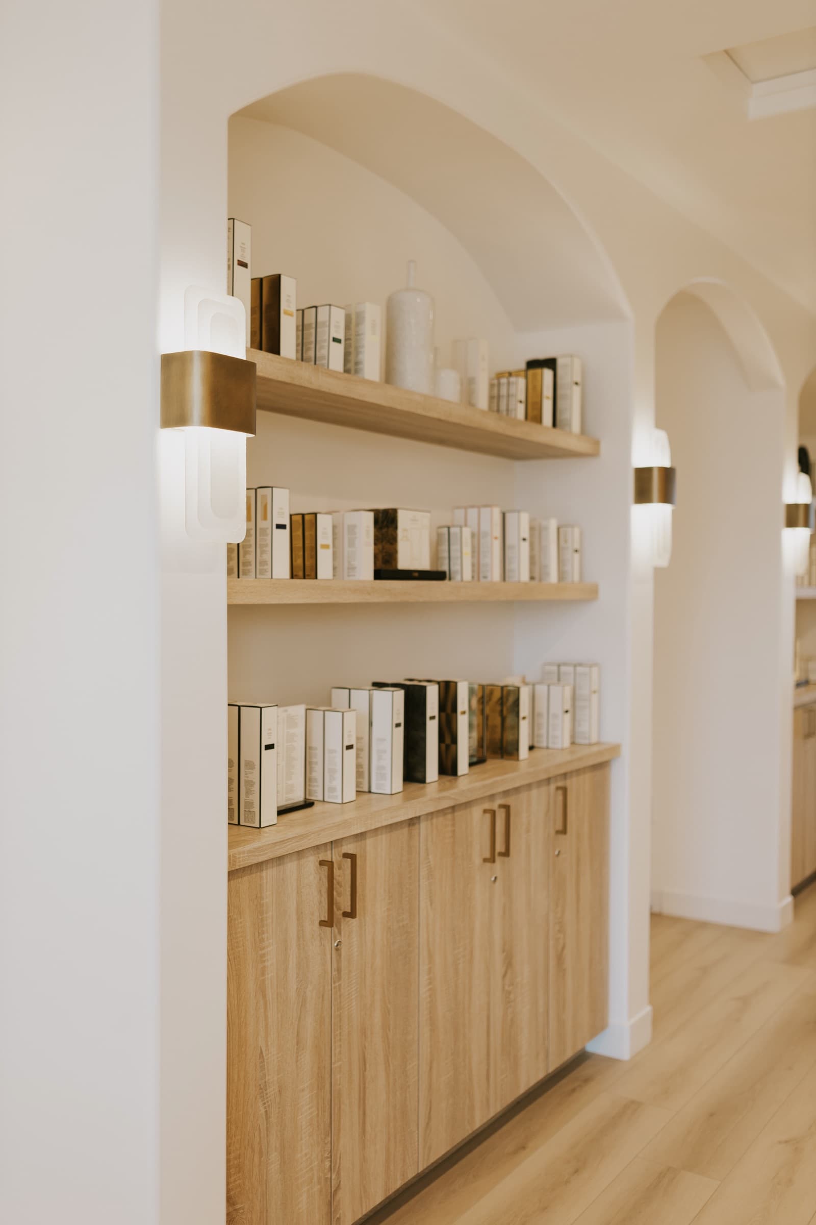 Retail shelving beneath an arched alcove, stocked with haircare in brass-topped canisters.