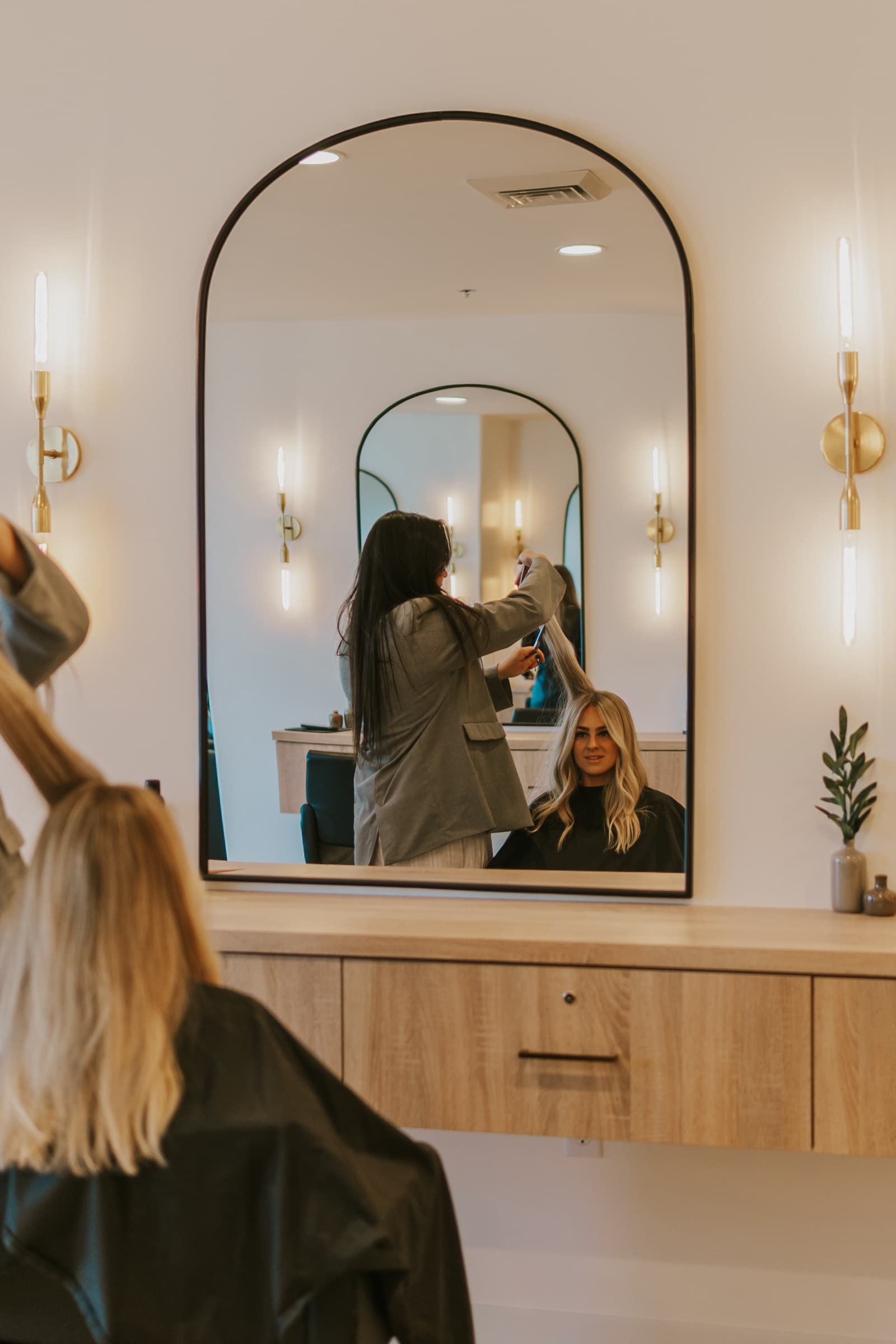 A stylist blow-drying a client's hair at an arched mirror station in the salon.