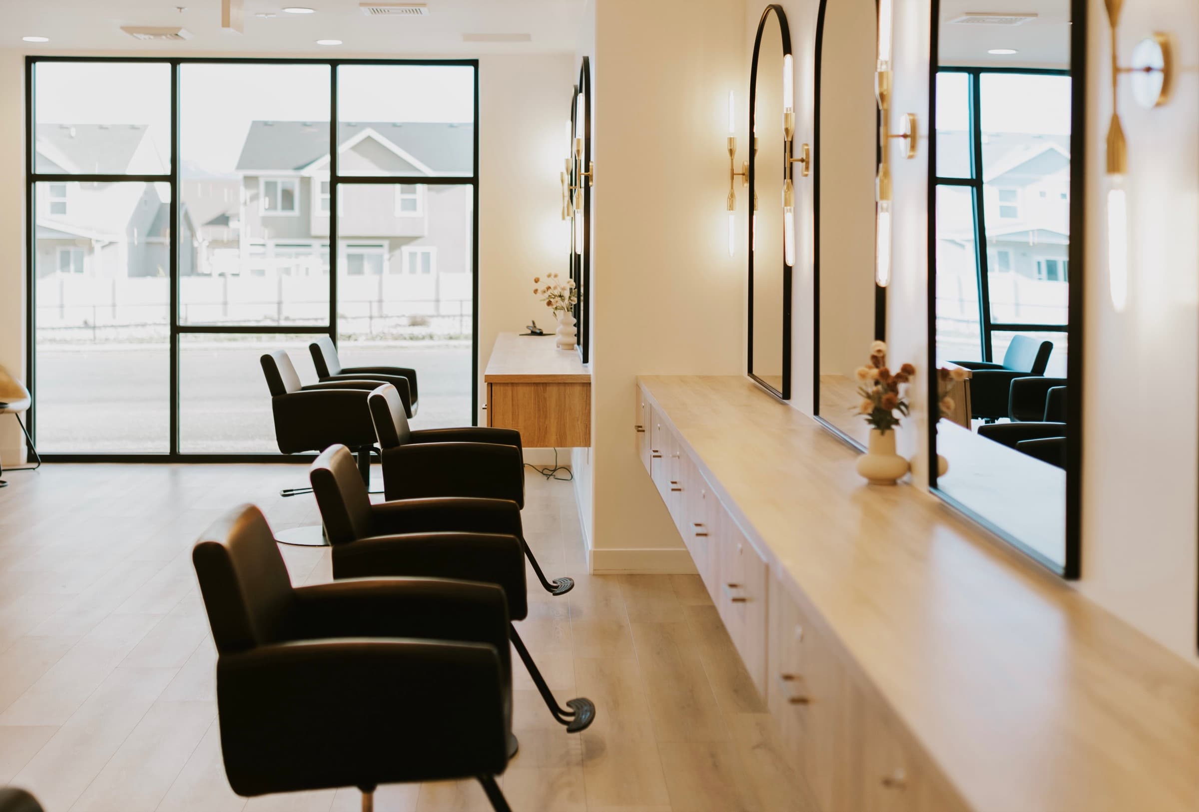 The Wilde Willow salon floor: a run of styling chairs facing a long oak counter and arched mirrors, with tall windows along one wall.