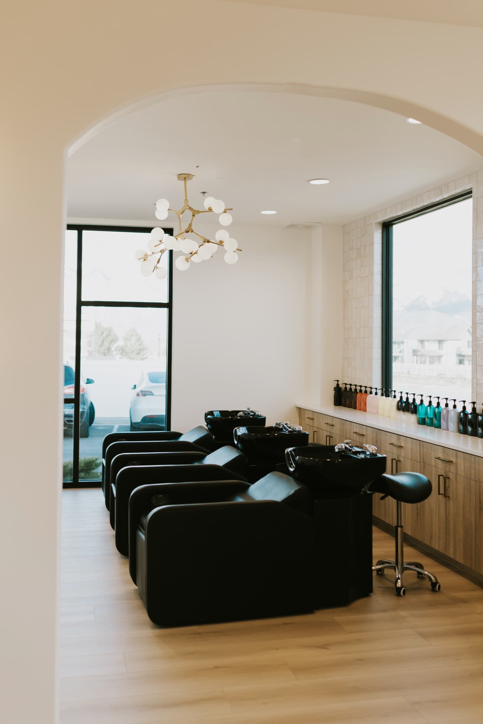 The wash area at Wilde Willow, with shampoo chairs beneath an arched entry and a brass chandelier.